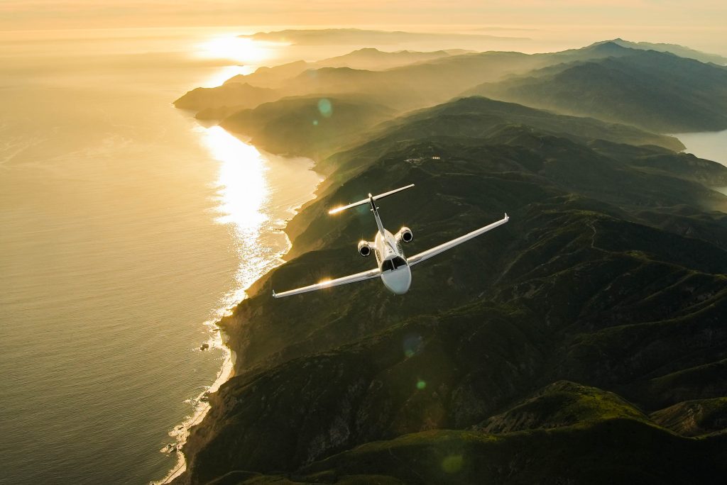 private jet plane type: entry level jet flying over sea and mountainous coastline during sunset