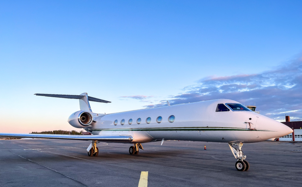 A large white private jet from the right front side parked on the ground on a clear day