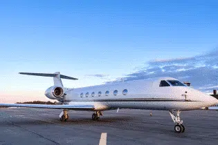 A large white private jet from the right front side parked on the ground on a clear day