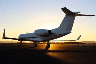 A large white private jet from the left back side parked on the ground on a clear day during sunset