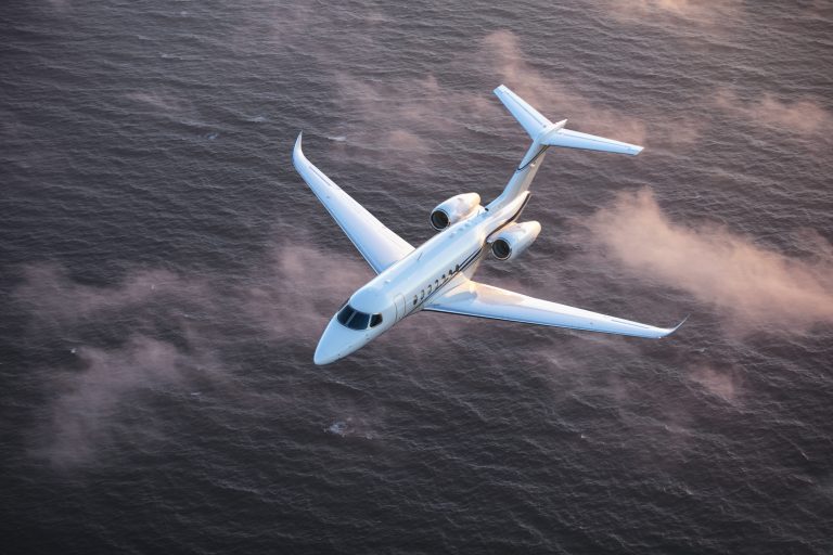 a white private jet flying over sea