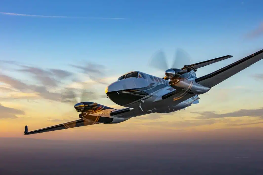 A executive white and black painted turboprop airplane with two engines flying before sunset