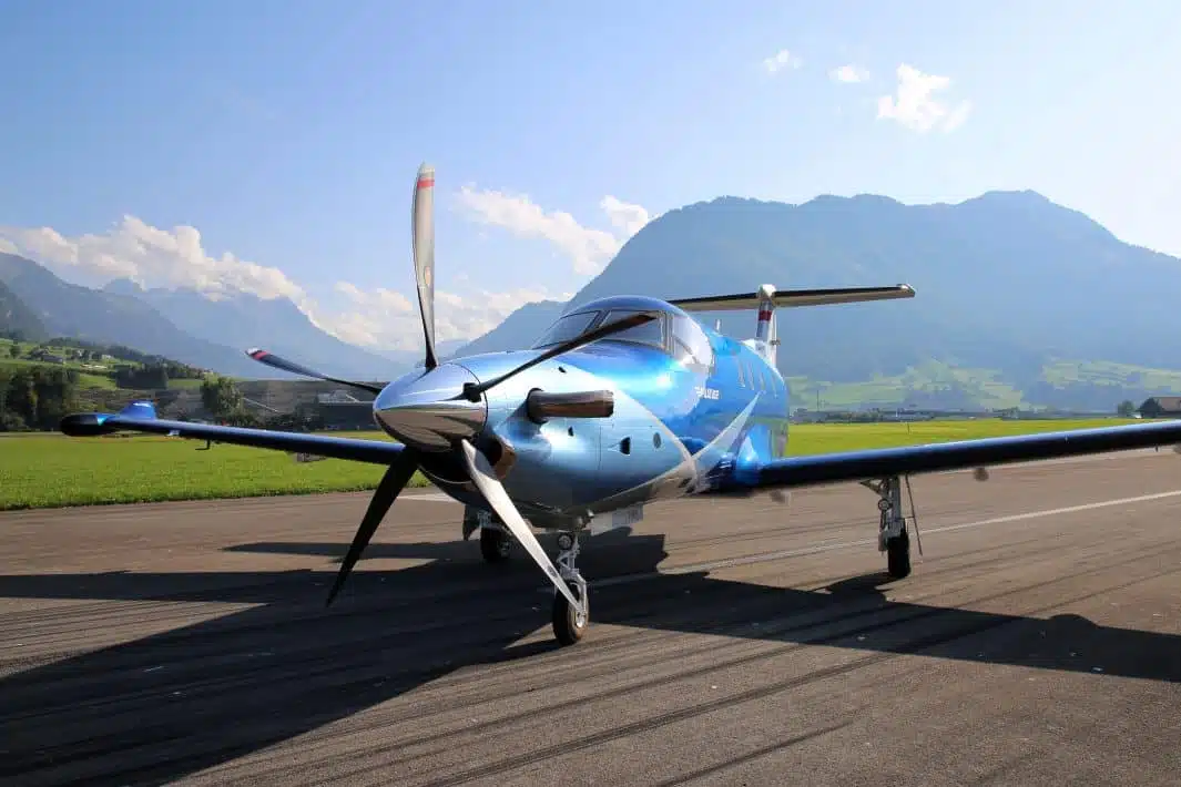 A blue painted executive turboprop airplane with one engine parked on the ground between the mountains