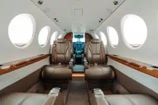 The interior of a private jet with a white and brown finish and brown leather seats