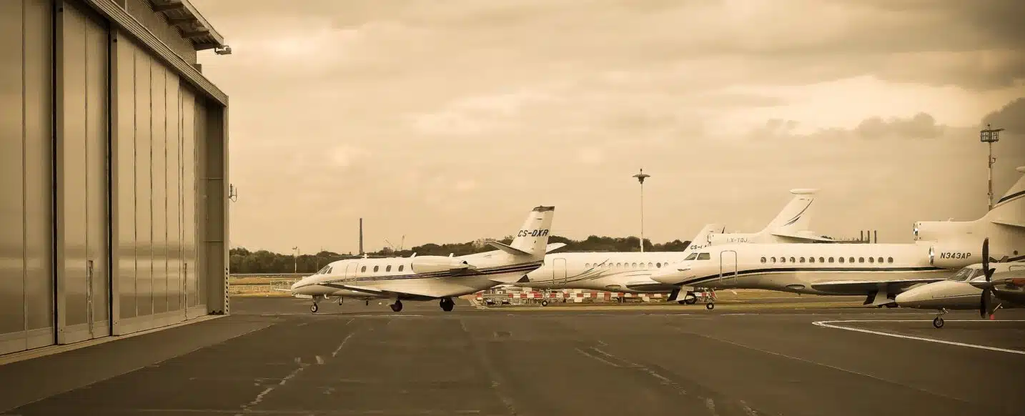 a picture in sepia style showing multiple private jet charter aircraft parked on the asphalt next to a hangar at the airport