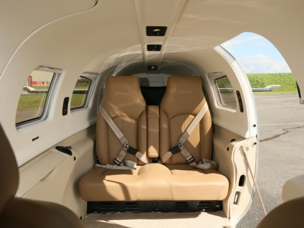 Interior view of a Pilatus PA-46 turboprop aircraft cabin with two tan leather seats, built-in side table, and overhead lighting.