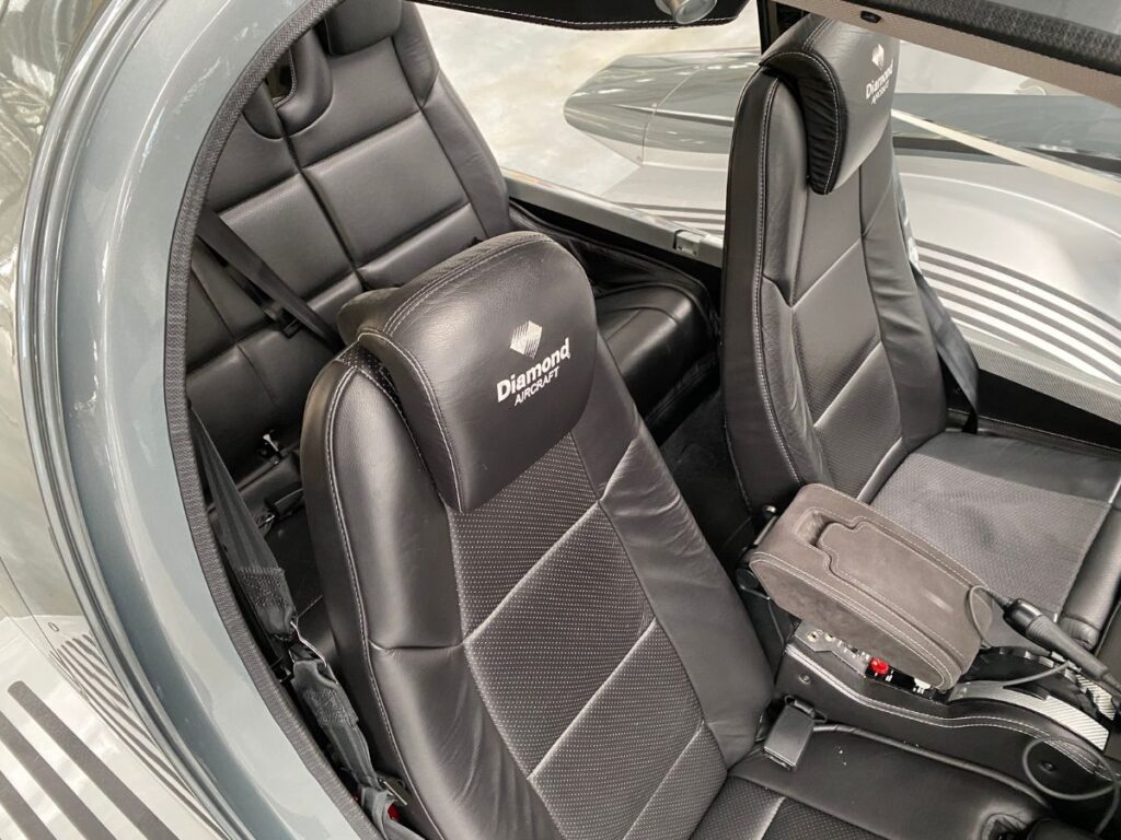 interior close-up picture of an airplane cabin. the dark black leather seats have a headrest with the diamond aircraft logo.