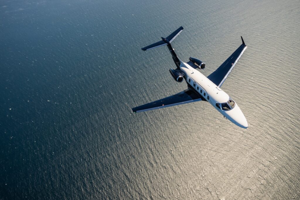 White Embraer Phenom 300 light jet flying over the sea, showcasing sleek design and modern executive aircraf