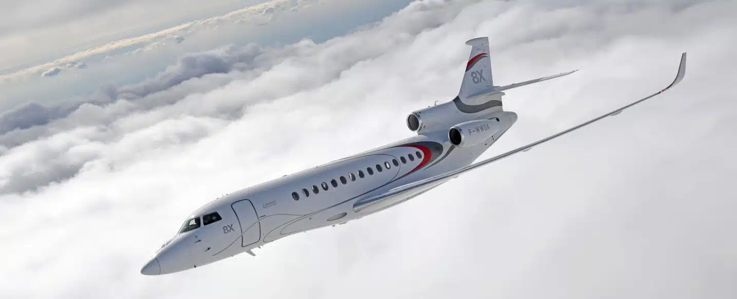 An all-white Dassault Falcon 8X business jet soaring above a thick cloud layer; showcasing long-range performance and sleek aerodynamic design.