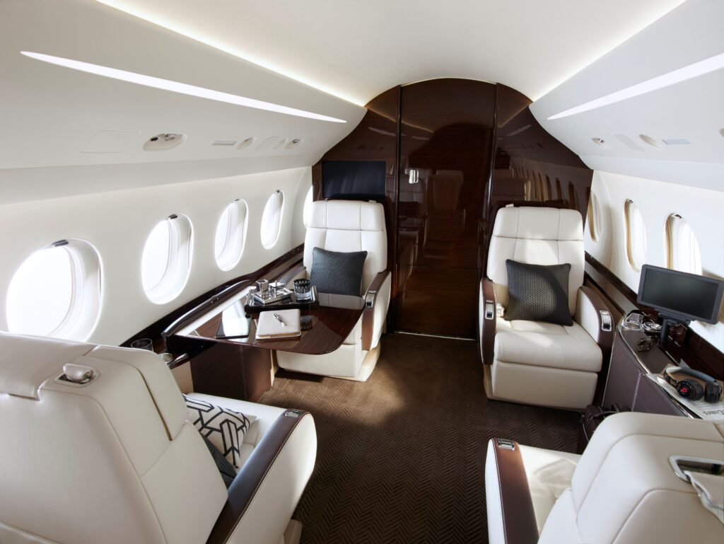 Modern and spacious private jet cabin interior with ergonomic white leather seating, premium wood grain accents, and natural window lighting.