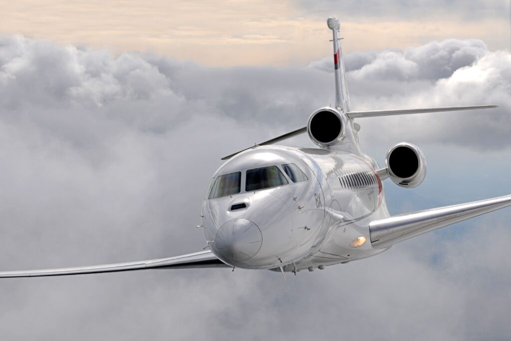 An all-white Dassault Falcon 8X business jet soaring above a thick cloud layer; showcasing long-range performance and sleek aerodynamic design.