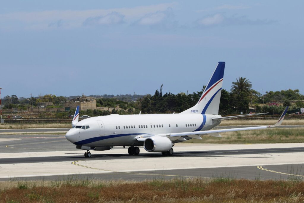 White BBJ private jet with blue stripes taxiing on the runway.