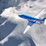 Bovenaanzicht van een blauwe Pilatus PC-24 vliegend boven de bergen.